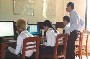 Photo: a computer class with a VI teacher teaching three students using computer